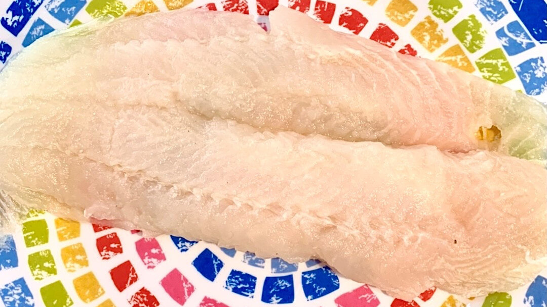 A large raw basa fish filet placed on a rainbow coloured dish, used to prepare a blackened basa recipe.