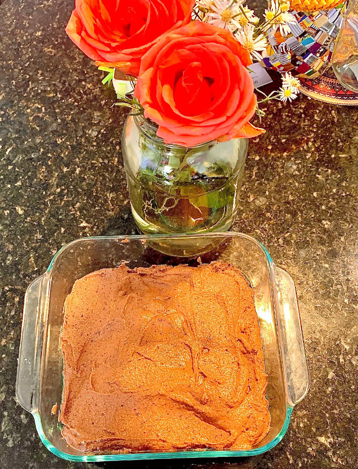 A finished tray of gluten free black bean brownies on a marble counter top next to an arrangment of red flowers